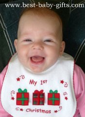 a smiling baby girl wearing a baby bib with 3 gift boxes on and saying "my 1st Christmas"