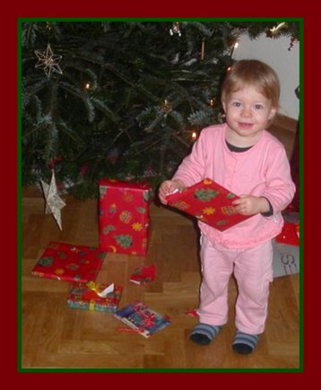 toddler girl in front of the Christmas tree holding a present