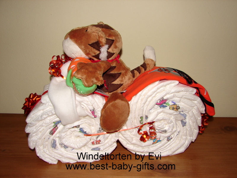 a cuddly tiger riding on a diaper motorcycle, the back of the motorbike is showcasing an orange Harley onesie