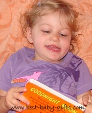 toddler laying on the floor, holding "Goodnight Moon" book and 'reading'