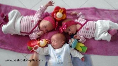 новорожденные тройняшки, лежащие на спине, наслаждающиеся обществом друг друга, 2 девочки в розовом, один мальчик в голубом