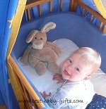 a baby girl looking up from her crib with a cuddly rabbit in the corner