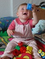 a baby girl dressed in a flower romper sitting on the floor playing with Lego Duplo