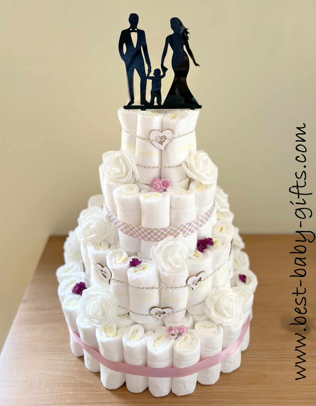 a large 4-tier diaper cake, wedding style, mostly white, with a cake topper showing the silhouettes of a wedding couple and a baby