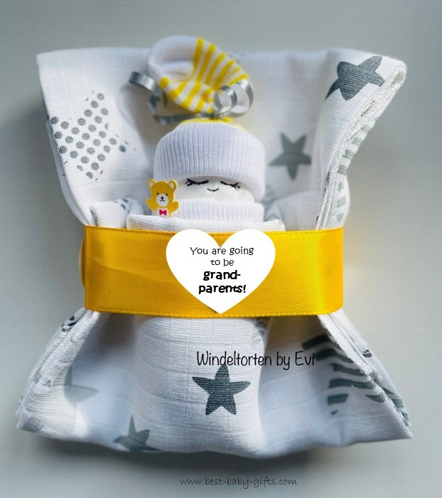 a little doll made of a diaper and yellow / white baby socks in  a sleeping bag (burp cloths) with a round sticker saying "You are going to be grandparents"