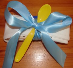 a onesie attached to a spoon with a blue ribbon, ready to stick to the diaper cake