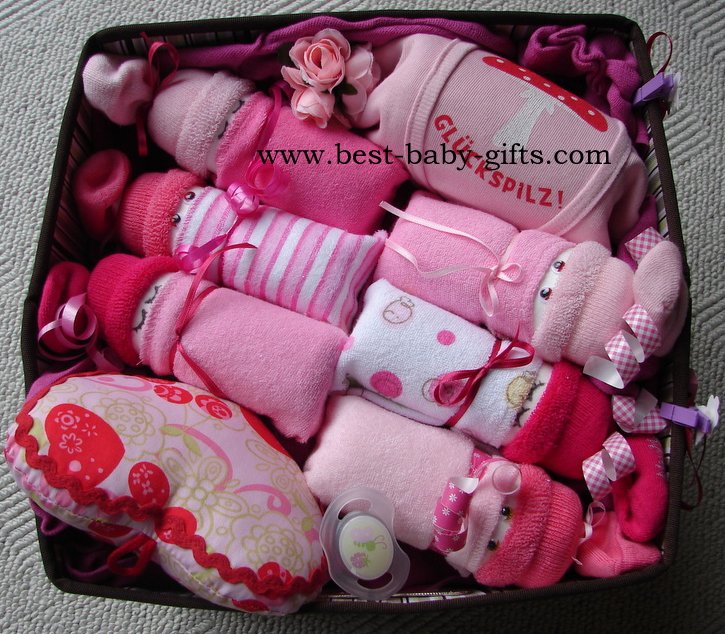 a big basket with 6 diaper babies, a baby onesie and a plush heart musical toy, all arranged nicely in the basket, pink colors