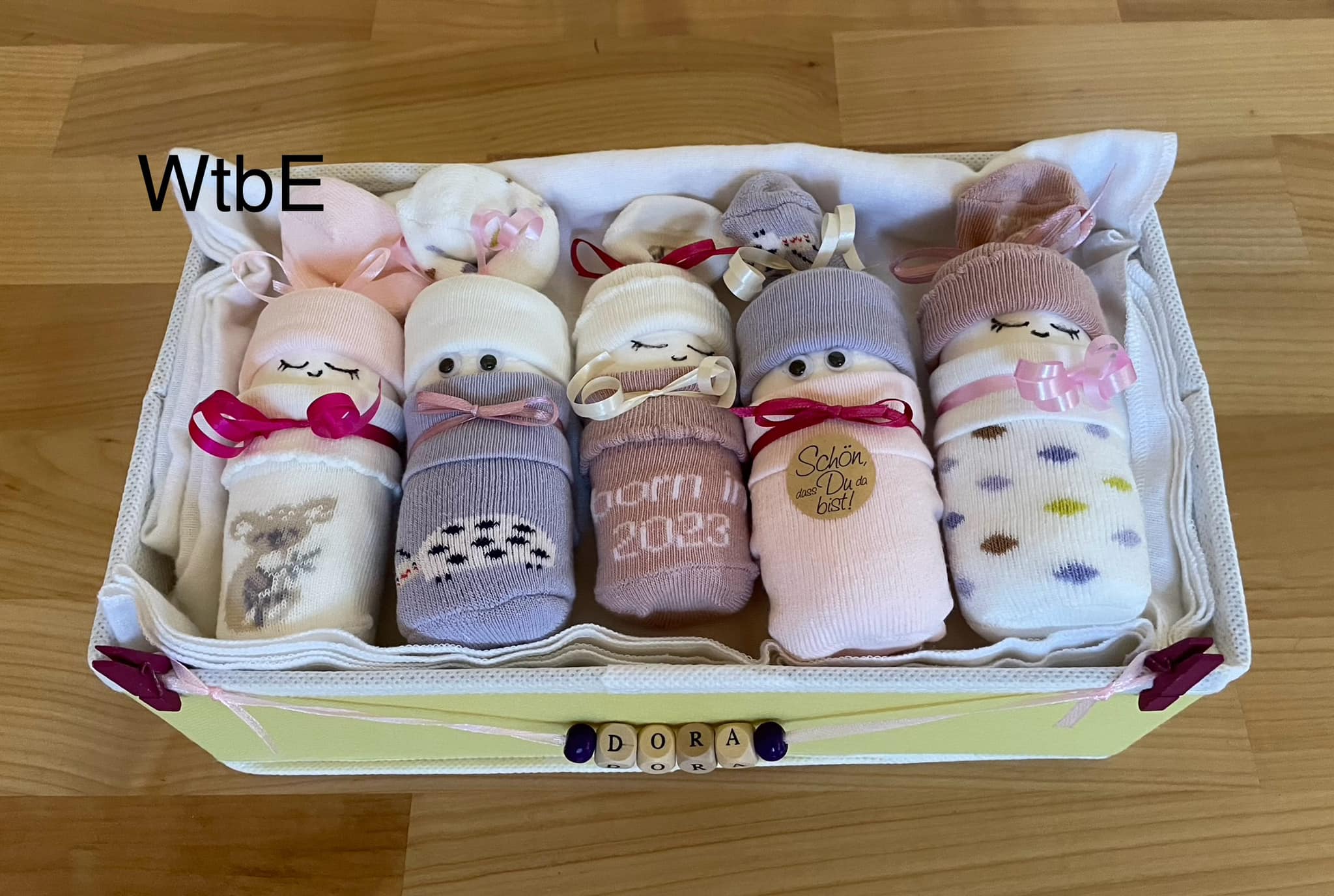 a yellow basket with 5 diaper babies in pink and violet colors for baby girl, personalized with wooden letters "Dora"