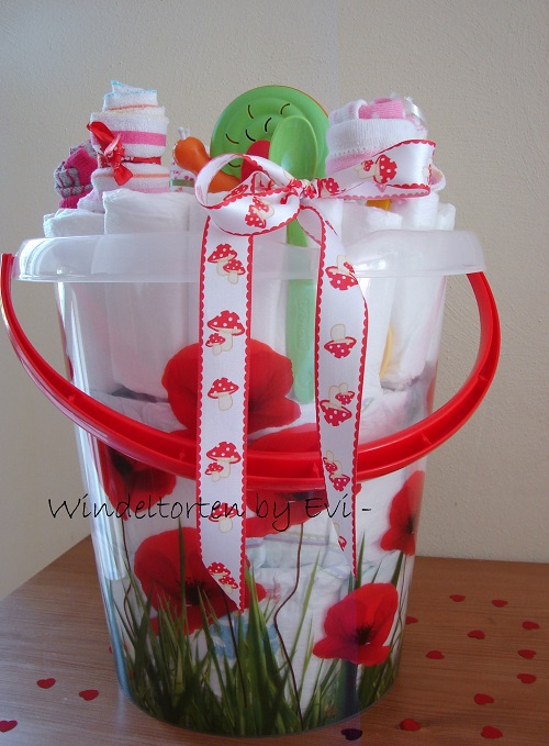 a large bucket with flower design filled with diapers and some baby items on top (rolled socks to make it look like flowers and a rattling snail toy)