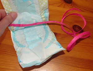fingers holding a diaper and pink ribbon inside