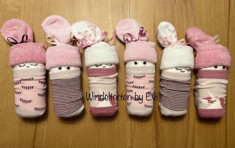 6 diaper sock babies in pink and rose shades, all lined up, each made of a diaper and a pair of socks