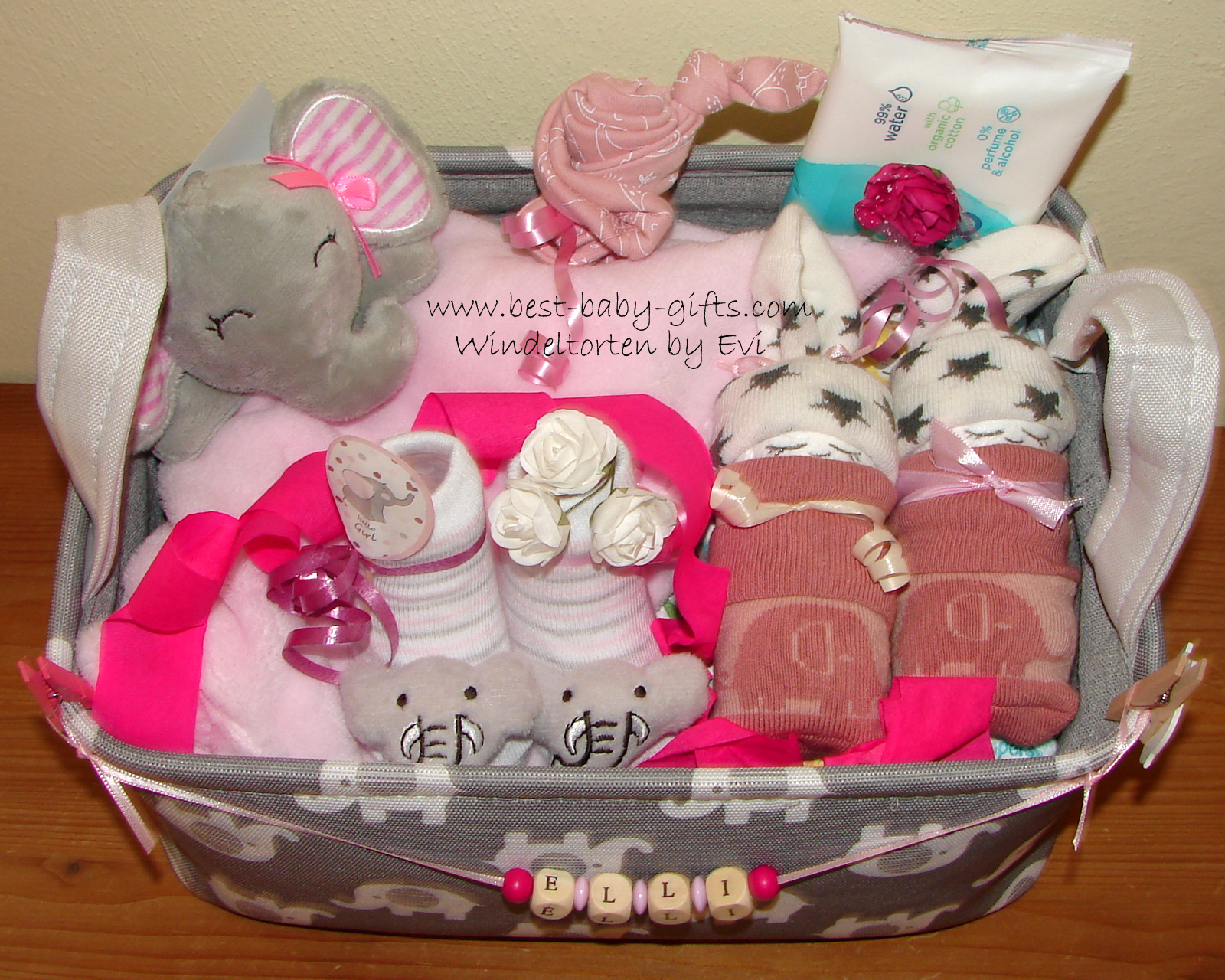 a gray storage basket with lots of elephant themed baby items on top, colors are all gray and pink for a baby girl, the basket is personalized with the name "Elli" in wooden letters on a ribbon