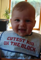 little girl wearing a bib saying 'cutest kid on the block'