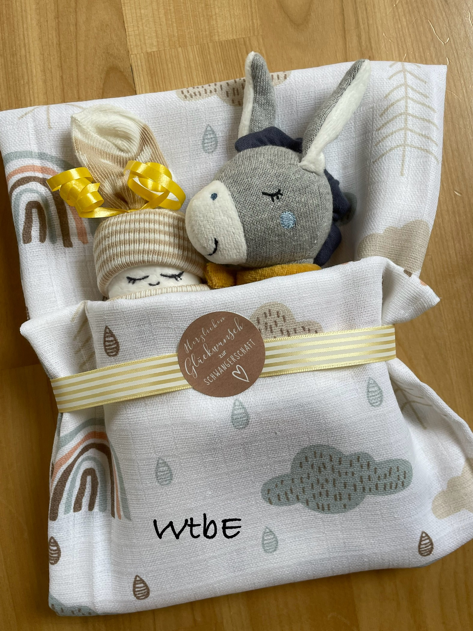 Geschenk zur schwangerschaft: ein Windelbaby und ein Esel sind in ein Tuch gewickelt, mit Sticker "herzlichen Glückwunsch zur Schwangerschaft", neutrale Farben weiss, grau, beige