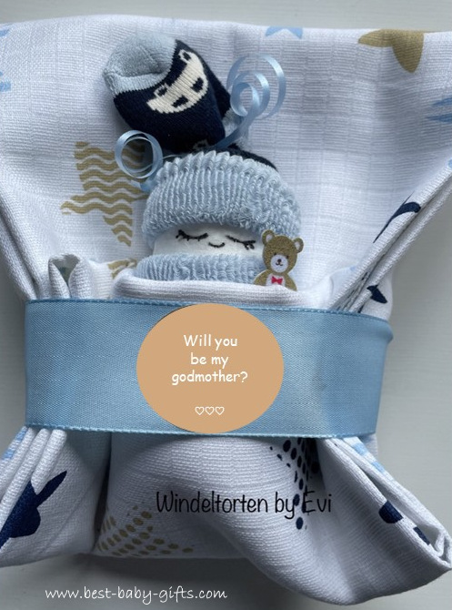 a blue diaper baby in a burp cloth with a sticker saying: will you be my godmother?