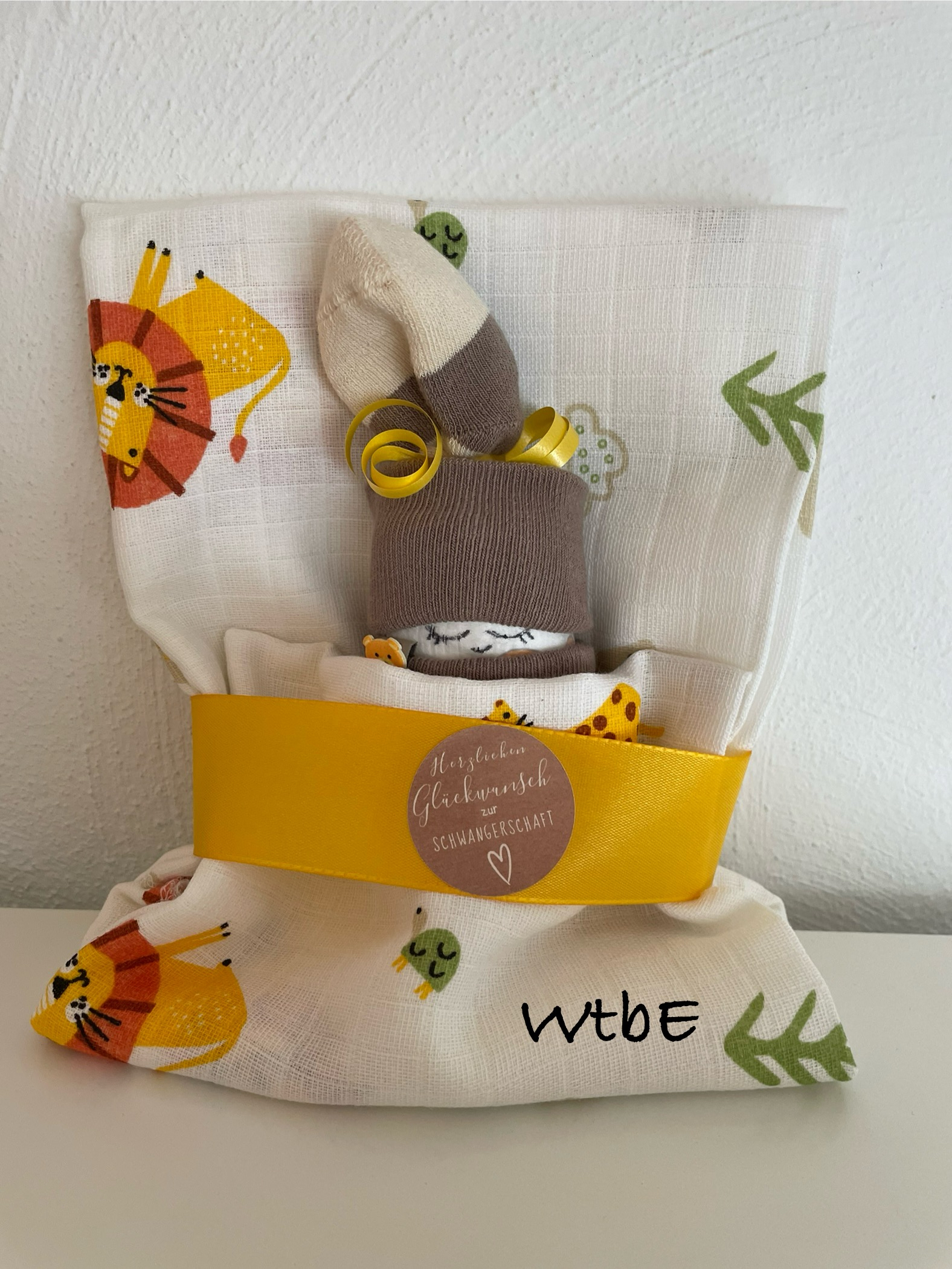 Windelbaby im Tuch mit Sticker "Herzlichen Glückwunsch zur Schwangerschaft", Farben gelb, braun, creme, orange