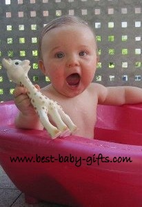 a little baby girl in a bath tub holding up Sophie the Giraffe