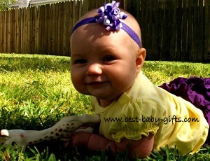 baby girl crawling on grass with Sophie the giraffe toy