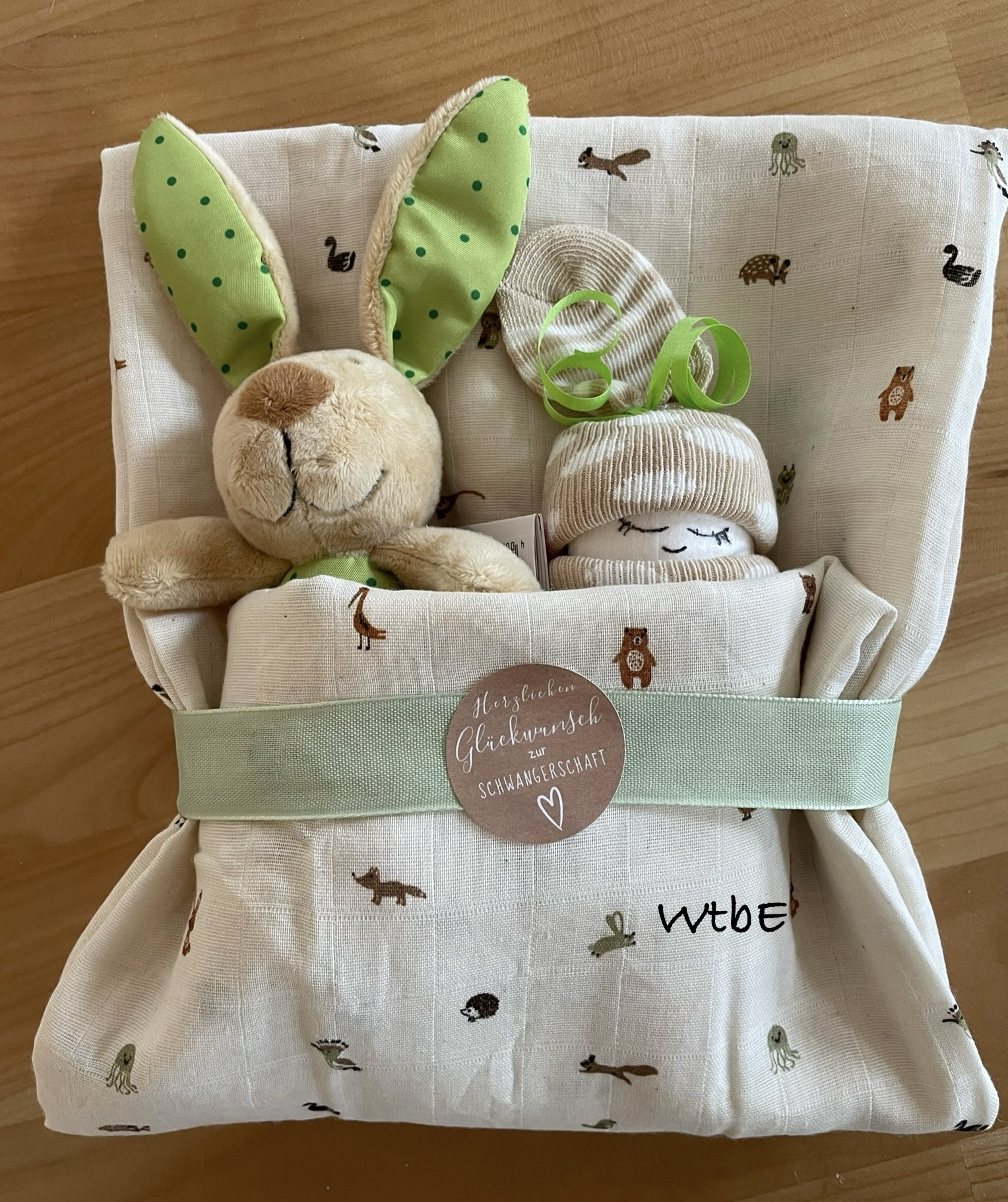 ein Windelbaby und ein Hase sind in ein Tuch gewickelt, mit Sticker "herzlichen Glückwunsch zur Schwangerschaft", neutrale Farben creme, beige, grün