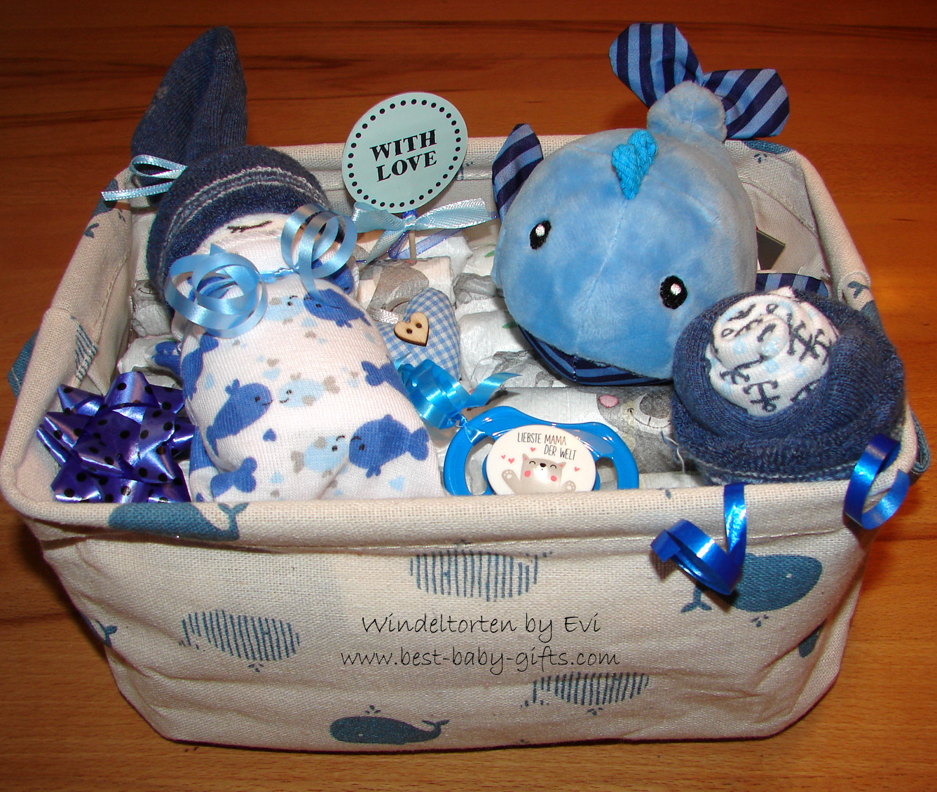 a little box with whale decor filled with a cuddly whale toy, a diaper baby, a pacifier, a "with love sign" and other small accessories