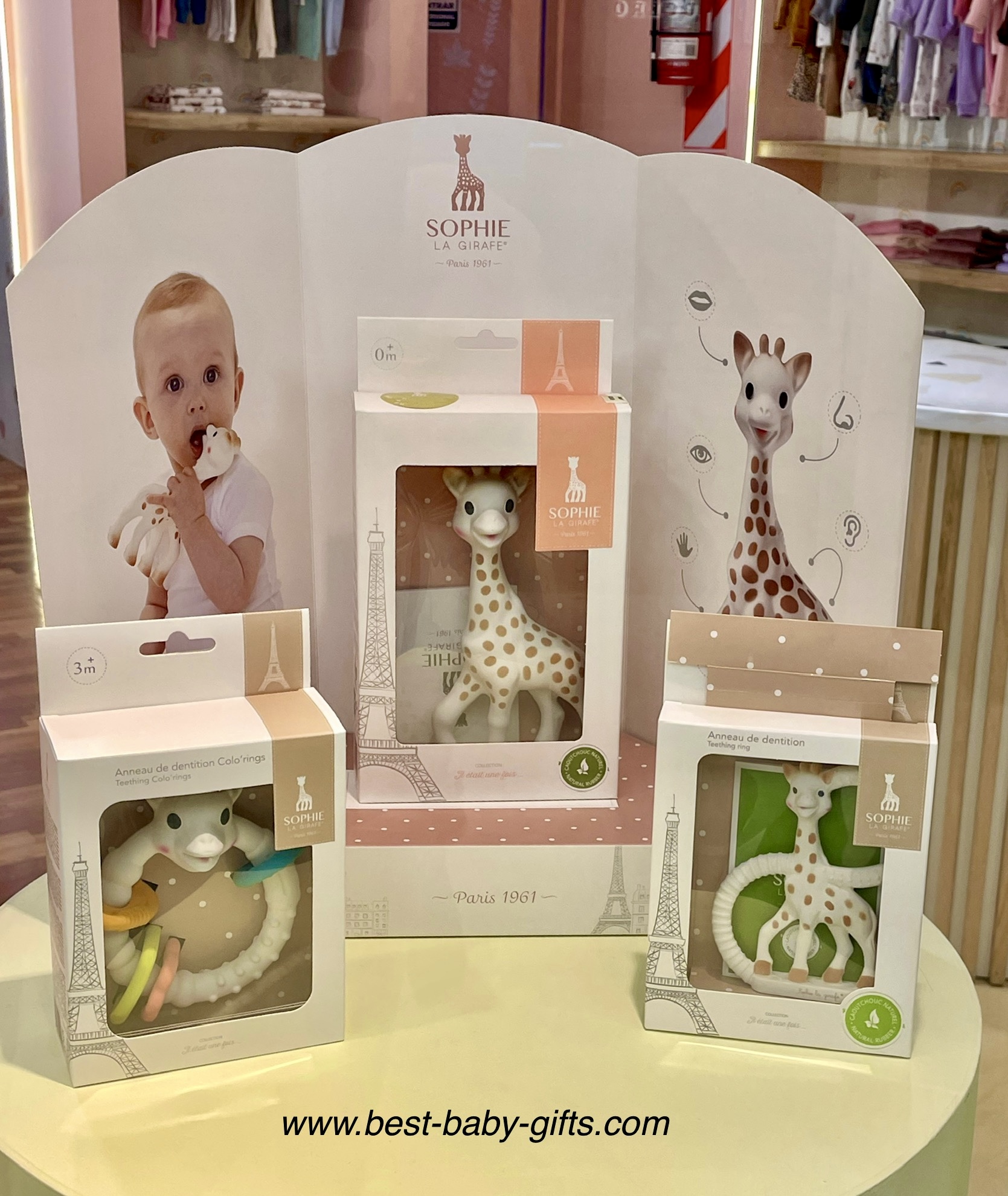 Sophie the giraffe gifts at a shop: Sophie teether, classic Sophie and Sophie ring toy, displayed on a little round table
