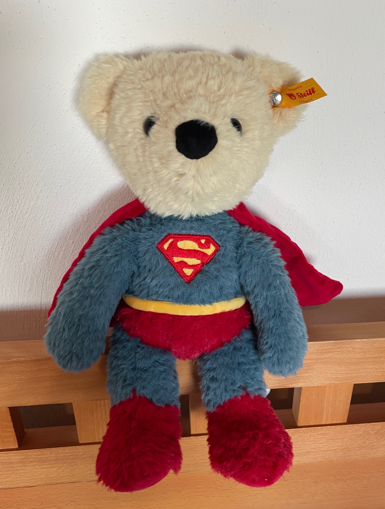Steff superhero teddy bear, a cuddly teddy bear wearing a superman outfit sitting on a baby bed frame