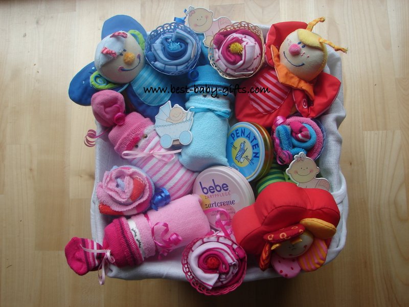 a large basket filled with diapers, 3 diaper babies on top as well as 3 rattles for newborn babies
