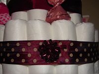 Windeln mit dunkelrotem Schmuckband mit weißen Punkten und aufgeklebter Fertigschleife um die 'Schnittstelle' zu verdecken