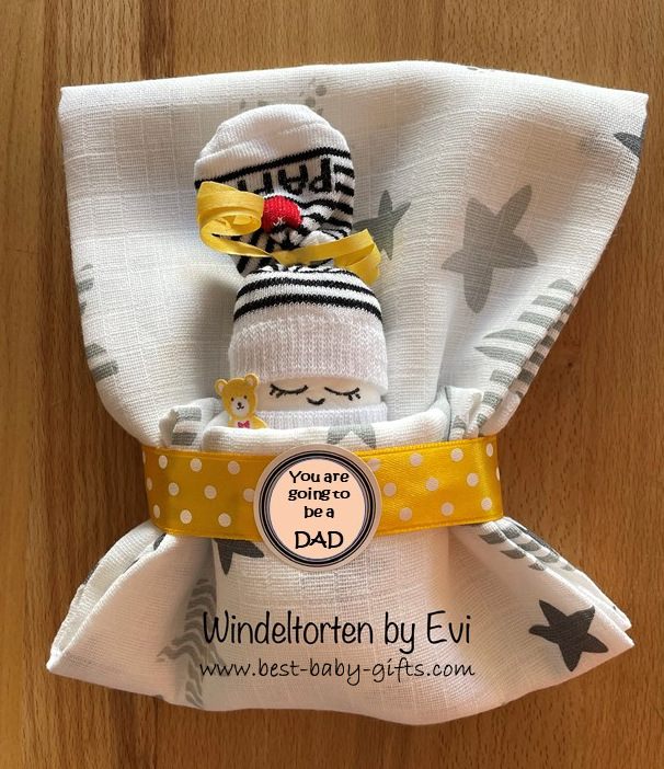a little doll made of a diaper and baby socks in  a sleeping bag (burp cloths) with a round sticker saying "You are going to be a dad"
