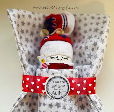 a little doll made of a diaper and red baby socks in  a sleeping bag (burp cloths) with a round sticker saying "You are going to be an aunt"